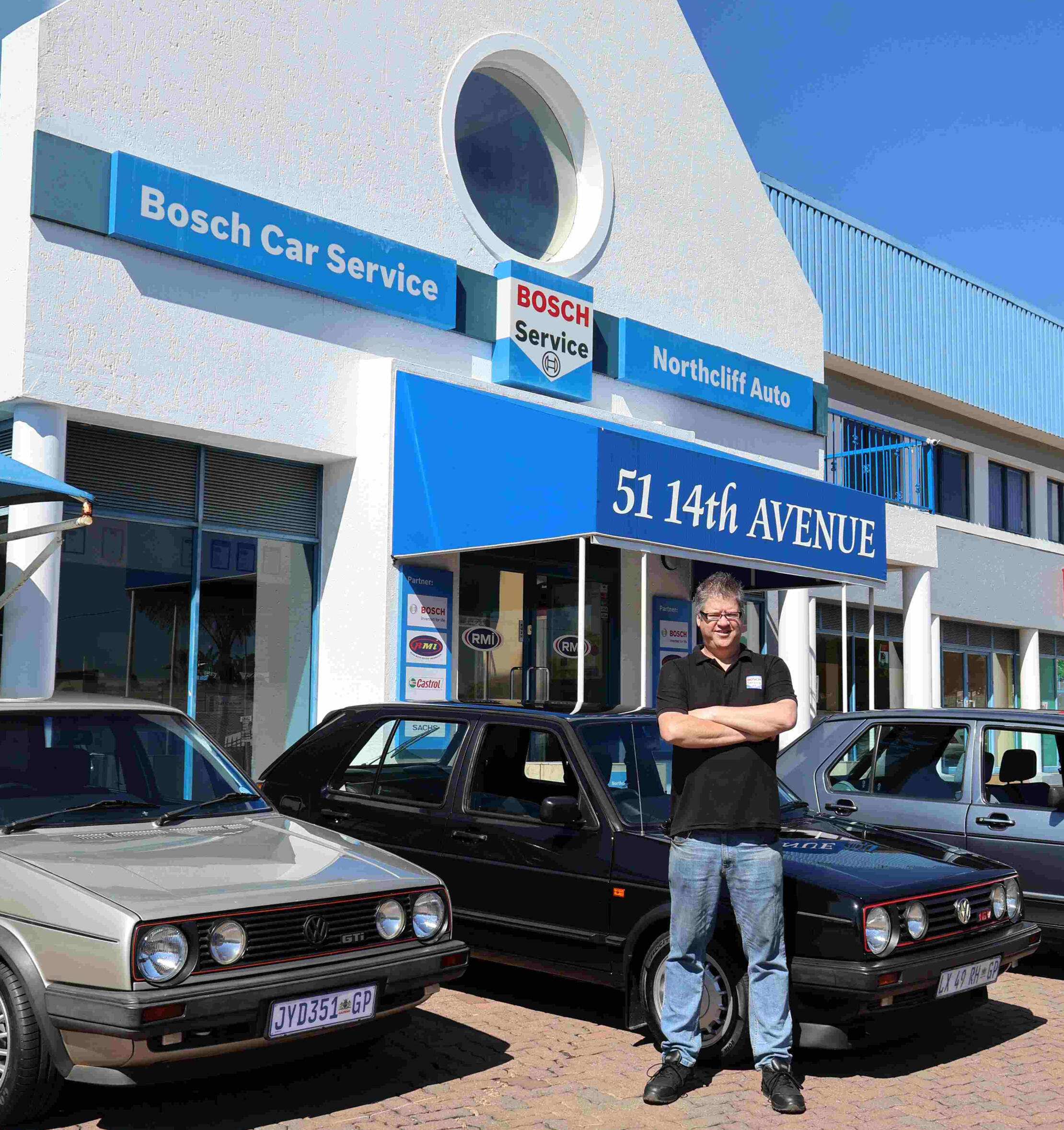 Manager Jacques Petzer standing outside of the Bosch Car Service Northcliff Auto building, standing infront of 3 popular VW cars.