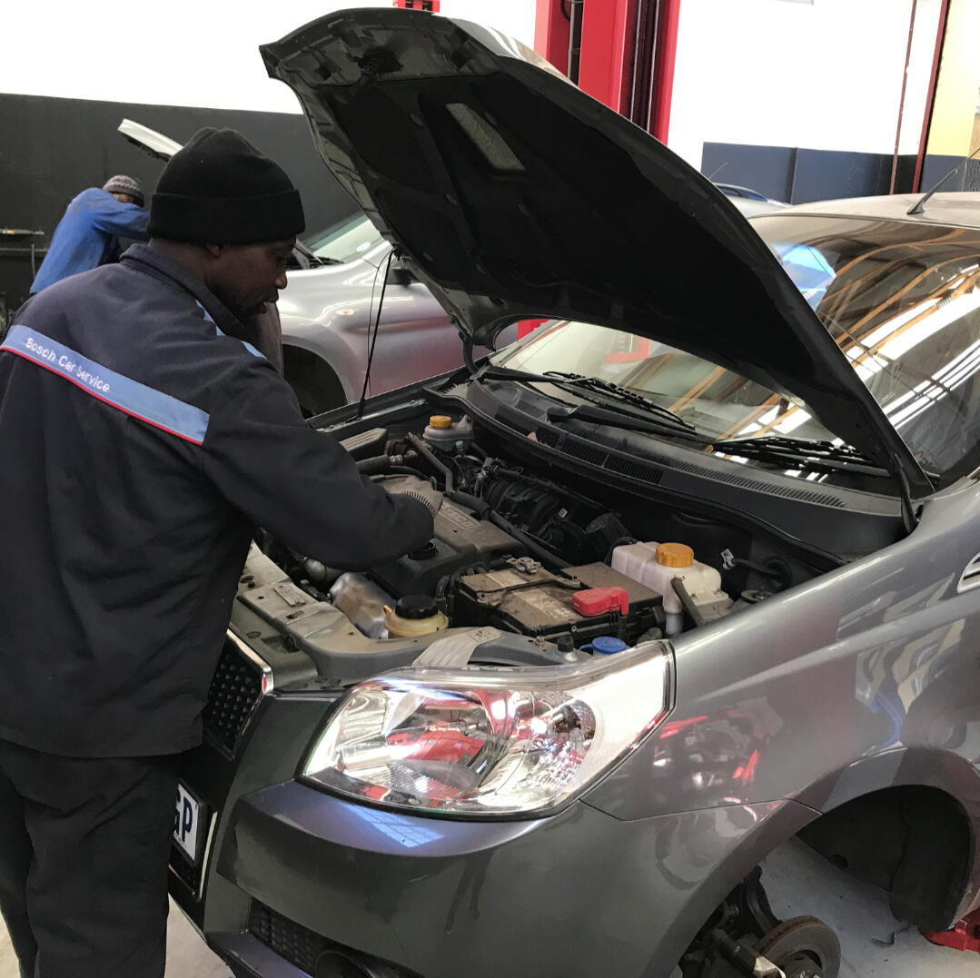 Man in Bosch Car Service uniform, servicing a dark grey car at Bosch Car Service Northcliff Auto